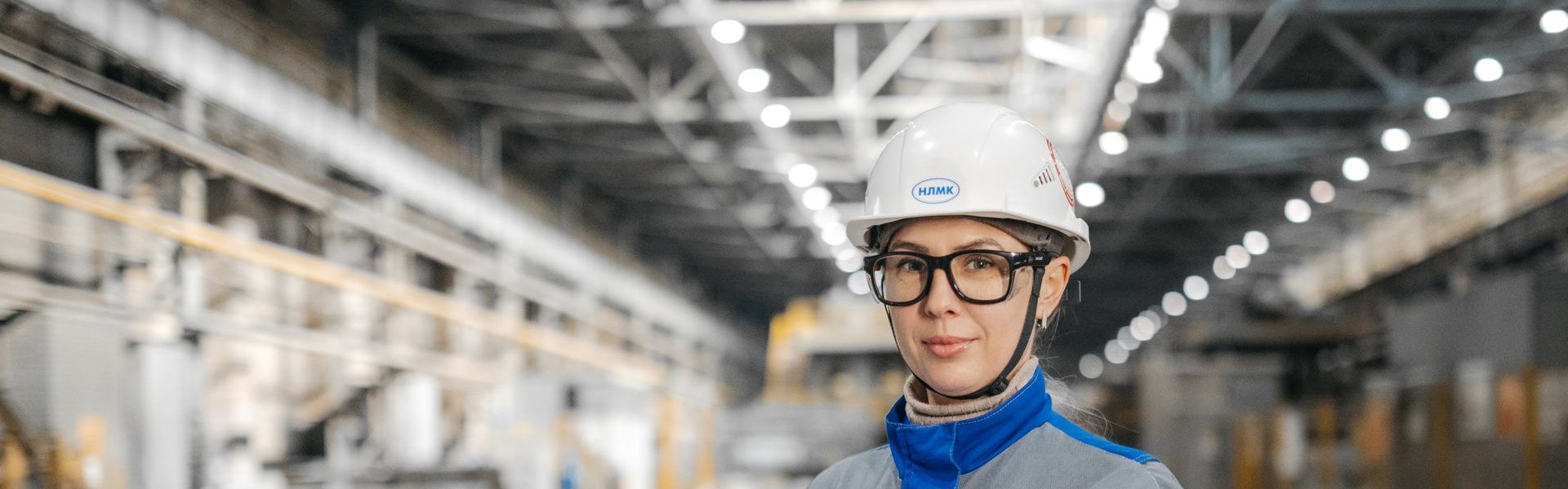 Health and safety professional in hard hat and safety glasses holding documents on a factory floor